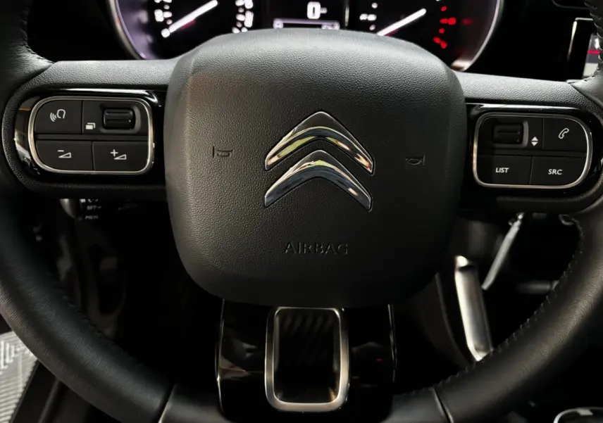 Gros plan sur le volant cuir noir du Citroën C3 Aircross 2024 avec commandes intégrées et logo chromé central.