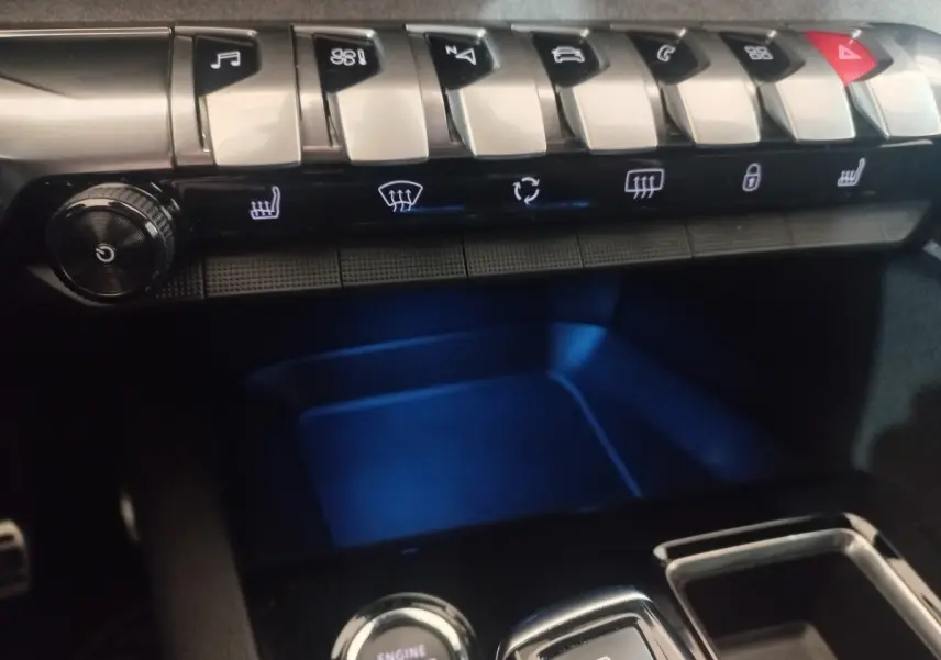 Gros plan sur la console centrale du Peugeot 3008 gris clair, avec boutons de contrôle et éclairage bleu intérieur.