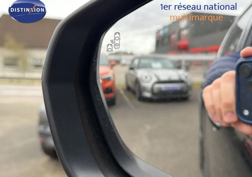 Rétroviseur côté droit d’un Citroën C5 Aircross noir métal 2025, avec reflet d’un parking et main tenant un smartphone.