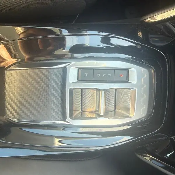 Vue plongeante sur la console centrale noire brillante de la Peugeot 208 Hybrid 110 e-DCS6 Allure 2024 avec commandes de boîte automatique.