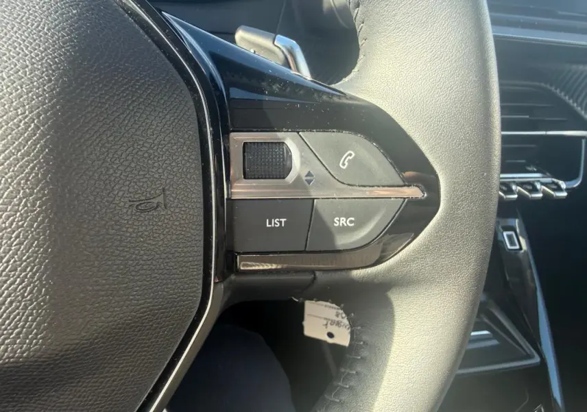 Gros plan sur les commandes gauche du volant noir de la Peugeot 208 Hybrid 110 e-DCS6 Allure 2024, intérieur moderne.