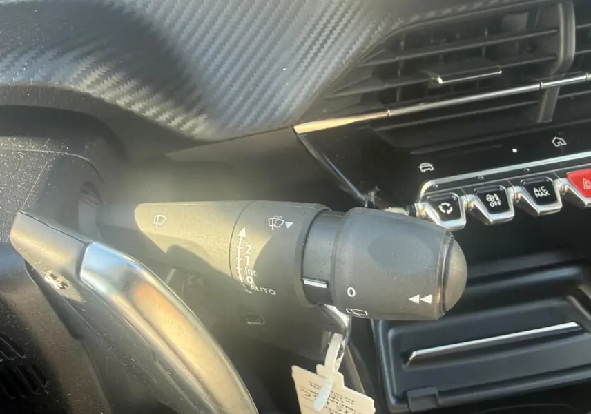 Gros plan sur la commande d’essuie-glace côté gauche du tableau de bord d’une Peugeot 208 Hybrid 110 e-DCS6 Allure blanche 2024.