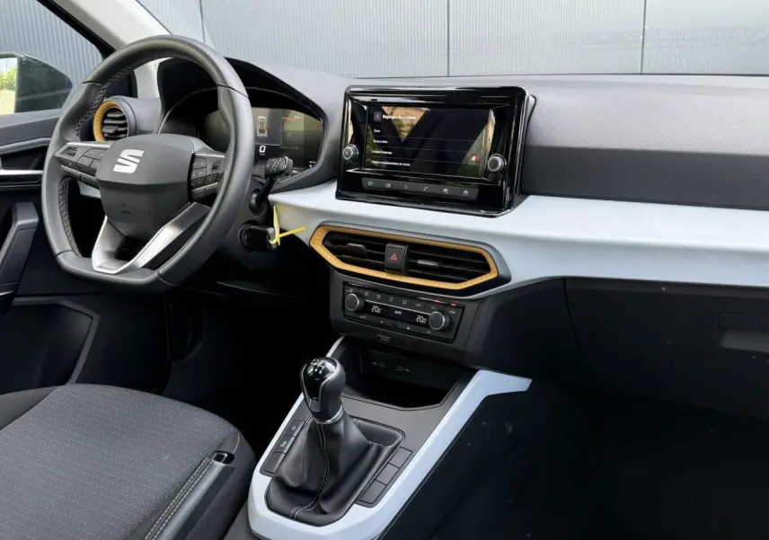 Vue intérieure côté conducteur du tableau de bord gris clair et noir du SEAT Arona TSI 115 avec volant multifonction et écran tactile central.