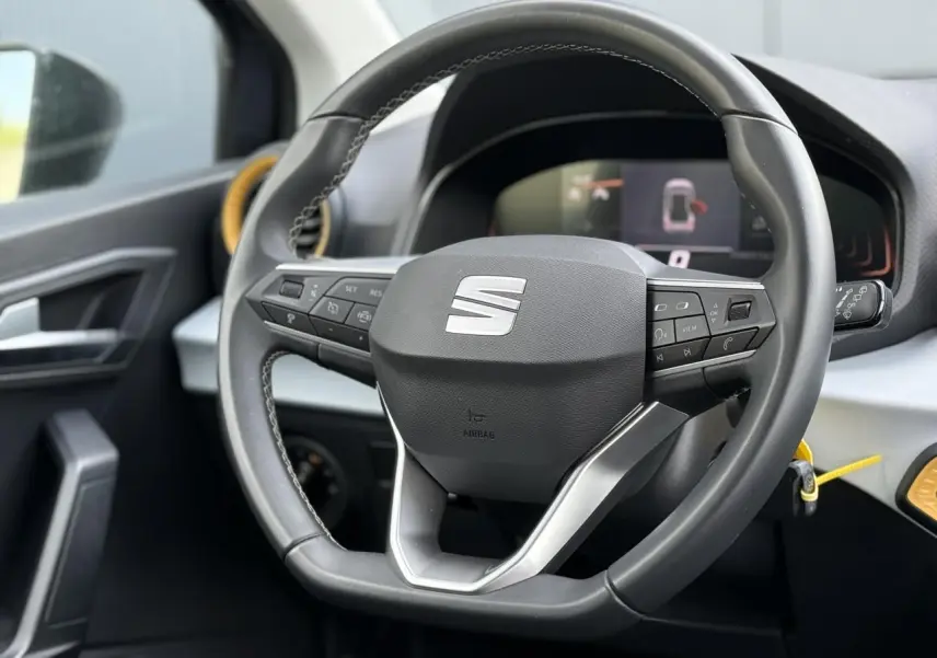 Vue rapprochée du volant multifonction noir du SEAT Arona 2025 avec détails argentés et tableau de bord digital en arrière-plan.