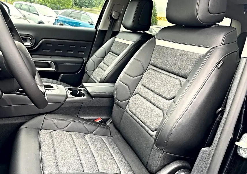 Vue intérieure côté conducteur du Citroën C5 Aircross 2025 noir, sièges tissu et cuir avec accoudoir central.