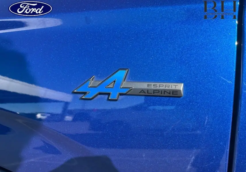 Gros plan sur l'emblème Esprit Alpine bleu sur la carrosserie Bleu Iron d'une Renault Austral 2023.