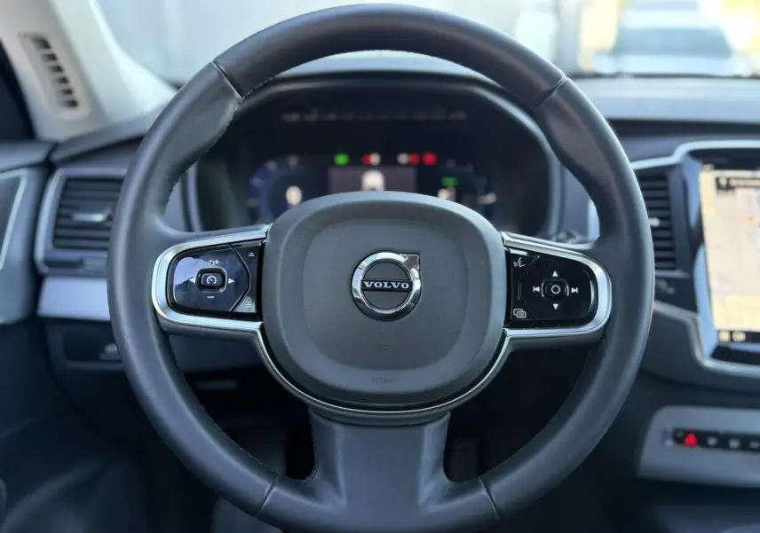 Volant noir de Volvo XC90 T8 2024, vue frontale centrée sur commandes et tableau de bord digital.