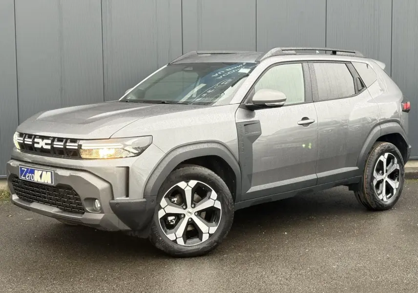 SUV Dacia Duster gris schiste en 3/4 avant droit, avec jantes alliage diamantées et barres de toit noires.