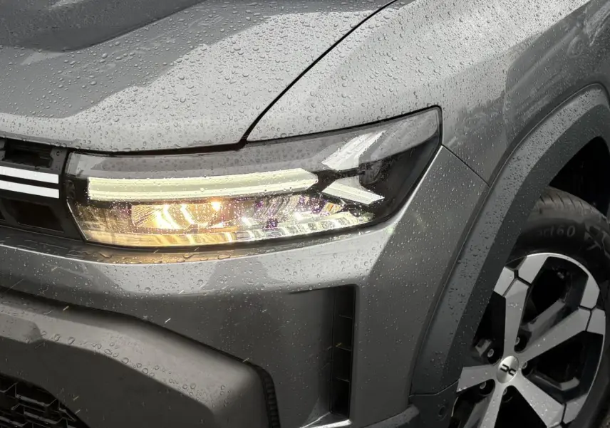 Gros plan sur l’avant droit du Dacia Duster gris Schiste, mettant en valeur le phare LED et la jante alliage diamantée.