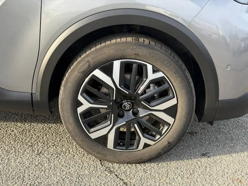 Gros plan sur la roue avant droite du Citroën C4 X 2025 gris Mercury, avec jante alliage au design géométrique noir et argent.