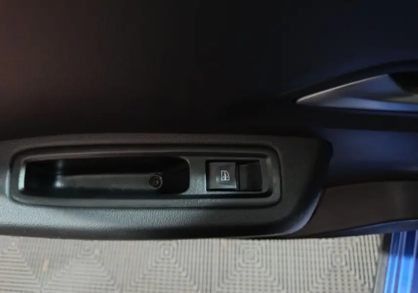 Détail de la commande de lève-vitre côté conducteur sur porte intérieure noire d'une Dacia Sandero bleu 2024.