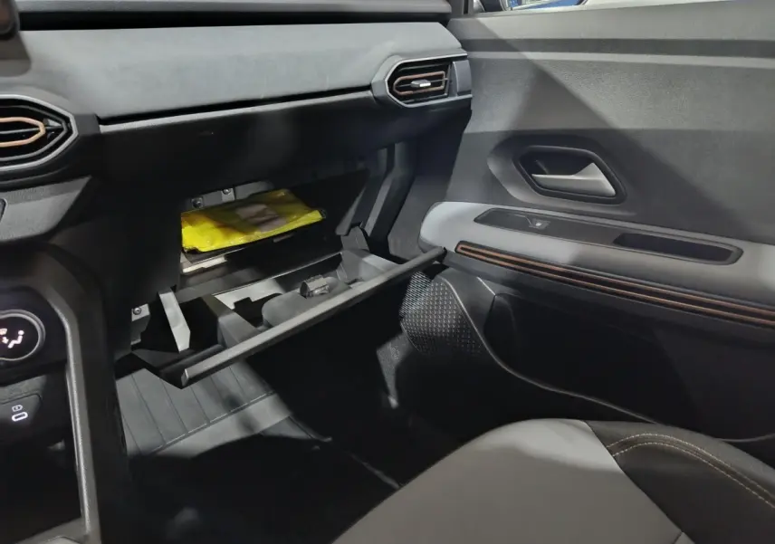 Vue intérieure côté passager du tableau de bord noir et gris avec boîte à gants ouverte sur Dacia Sandero Extreme+ bleu 2024.
