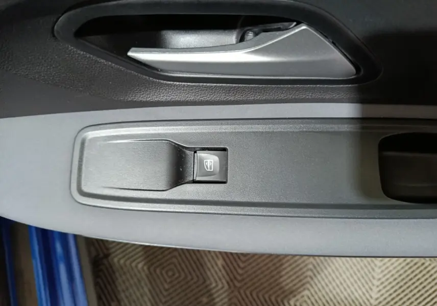 Détail de la commande de lève-vitre côté conducteur sur la portière intérieure grise d'une Dacia Sandero bleu 2024.