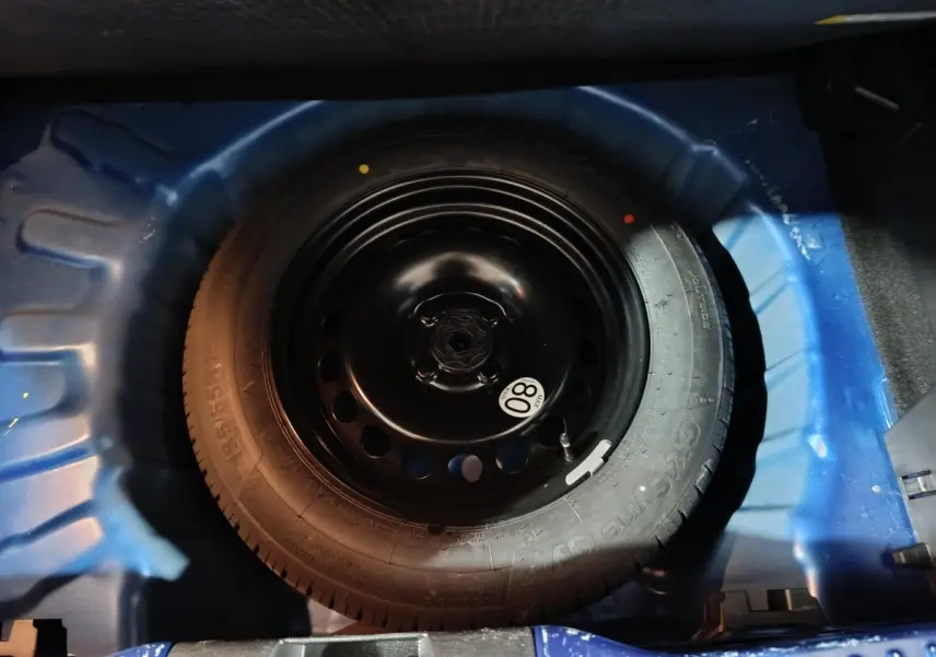 Gros plan sur la roue de secours galette noire dans le coffre bleu d'une Dacia Sandero 2024 Extreme+ TCe 110.