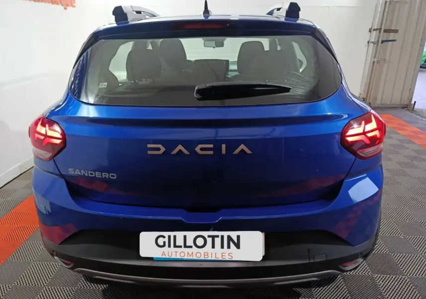 Vue arrière d'une Dacia Sandero bleu vif 2024, feux LED allumés et logo DACIA bien visible.