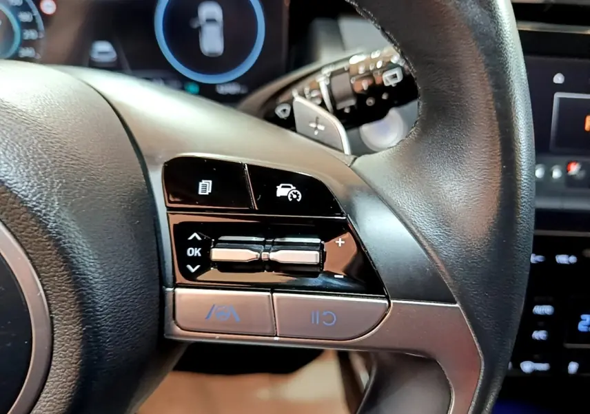 Gros plan sur les commandes du volant cuir noir du Hyundai Tucson 2022, avec boutons de régulateur de vitesse et assistance.