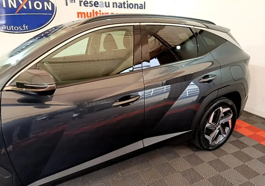 Vue côté gauche d’un Hyundai Tucson gris foncé 2022, mettant en valeur les jantes et la ligne de toit avec rails intégrés.