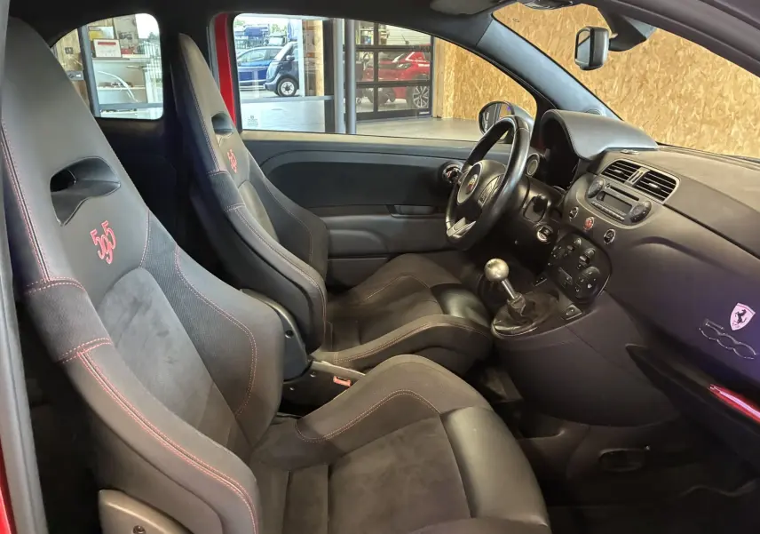 Vue intérieure côté conducteur de l'Abarth 500 Competizione 2016 rouge et gris, avec sièges sport numérotés et levier de vitesse manuel.