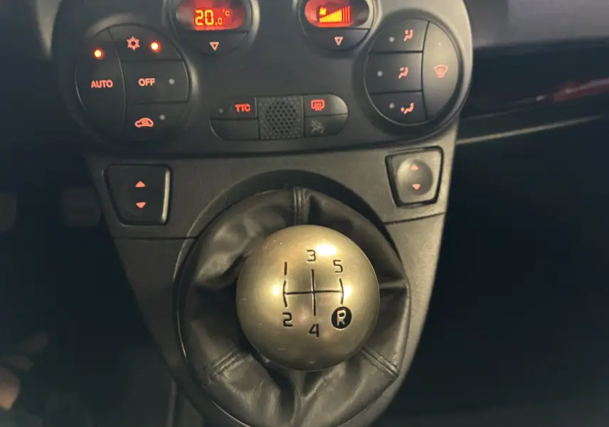 Gros plan sur le levier de vitesses manuel argenté et la console centrale avec commandes climatisation d’un Abarth 500 Competizione rouge et gris.