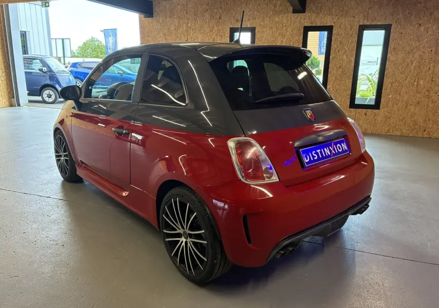 Vue 3/4 arrière gauche de l'Abarth 500 Competizione 2016 rouge et gris avec jantes noires en étoile, stationnée en intérieur.