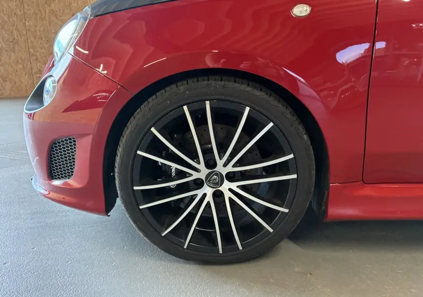 Gros plan sur la roue avant gauche de l'Abarth 500 Competizione 2016 rouge et gris avec jante noire à branches fines argentées.