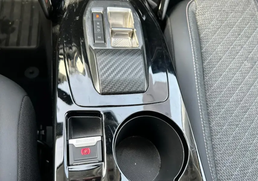 Vue rapprochée de la console centrale noire brillante avec levier de vitesse automatique et bouton de frein à main électrique sur Peugeot 208 gris.