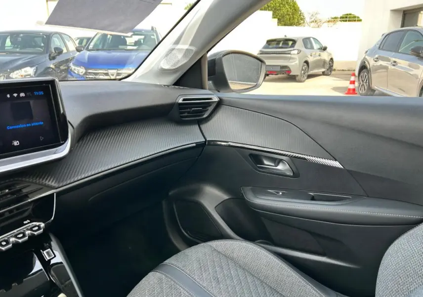Vue intérieure côté passager du Peugeot 208 Hybrid 110 e-DCS6 Allure 2024, avec tableau de bord noir et sièges gris.