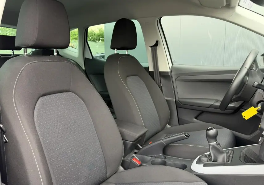 Vue intérieure avant du SEAT Arona 2025 TSI 115 Style, sièges tissu gris foncé avec boîte manuelle et accoudoir central.