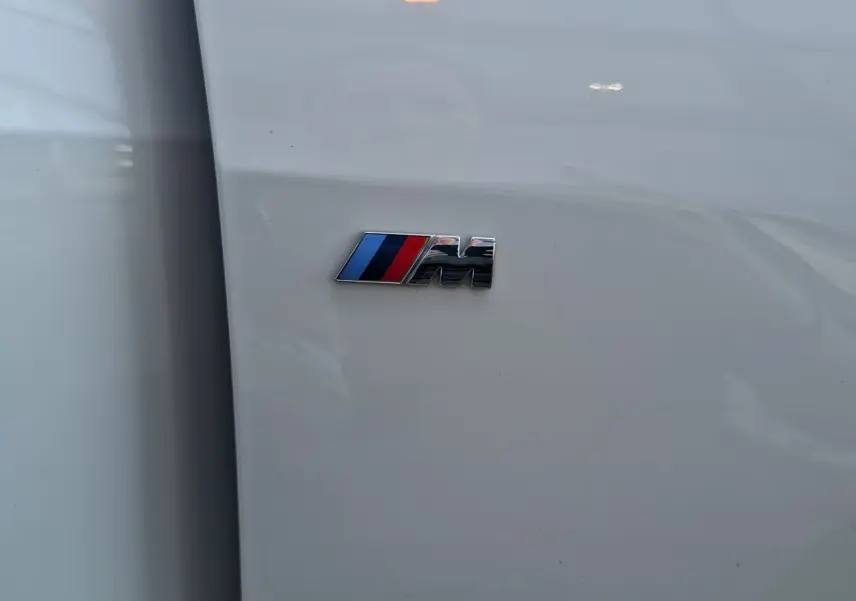 Détail du logo M sur la carrosserie blanche d'une BMW Série 1 118D M Sport, vue rapprochée côté gauche.