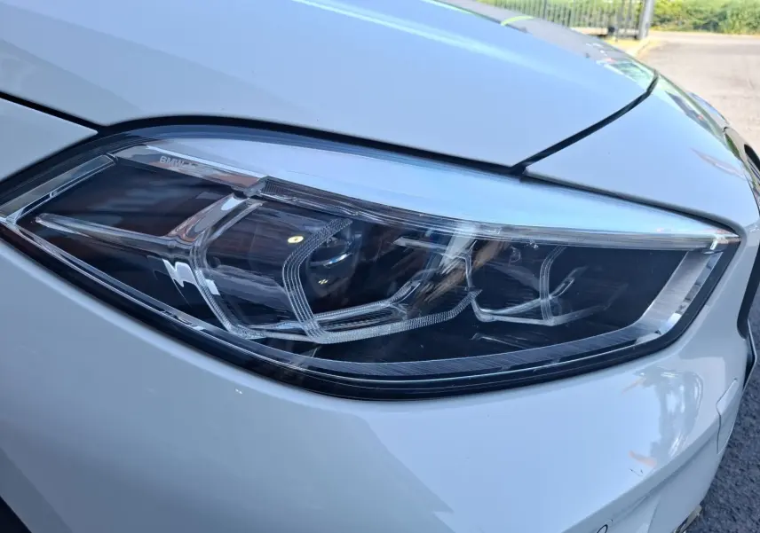 Gros plan sur le phare avant droit de la BMW Série 1 118D M Sport blanc, mettant en valeur ses détails LED modernes.