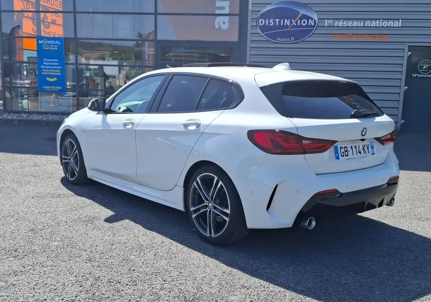 BMW Série 1 118D M Sport blanc vue 3/4 arrière droit, jantes alliage 18 pouces et vitres arrière surteintées.