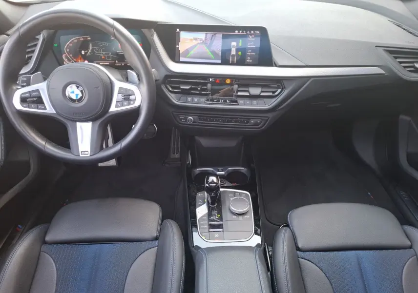 Vue intérieure avant de la BMW Série 1 118D M Sport blanche, avec volant multifonction, écran central et sellerie cuir/tissu.