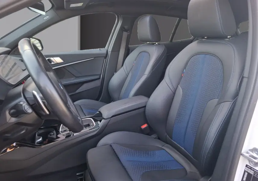 Vue intérieure côté conducteur de la BMW Série 1 118D M Sport blanc, sièges baquets cuir/tissu bleu et noir.