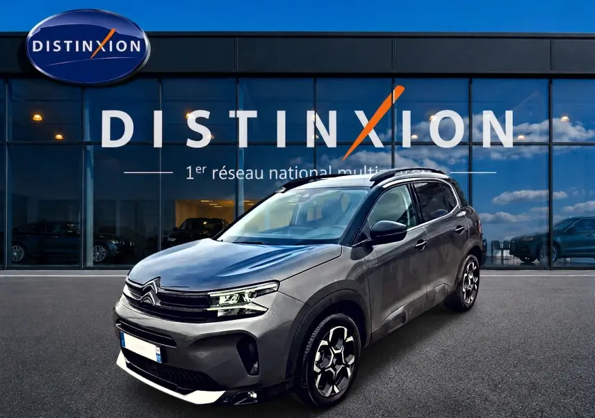 Citroën C5 Aircross gris en 3/4 avant droit, avec jantes alu et barres de toit visibles devant showroom Distinxion.