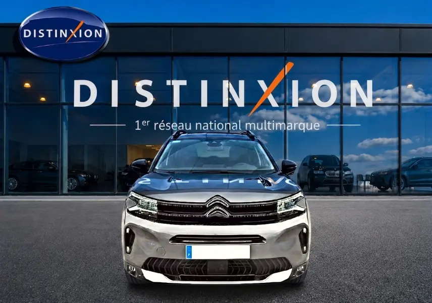 Citroën C5 Aircross gris vue de face, avec barres de toit et calandre distinctive, devant un showroom Distinxion.