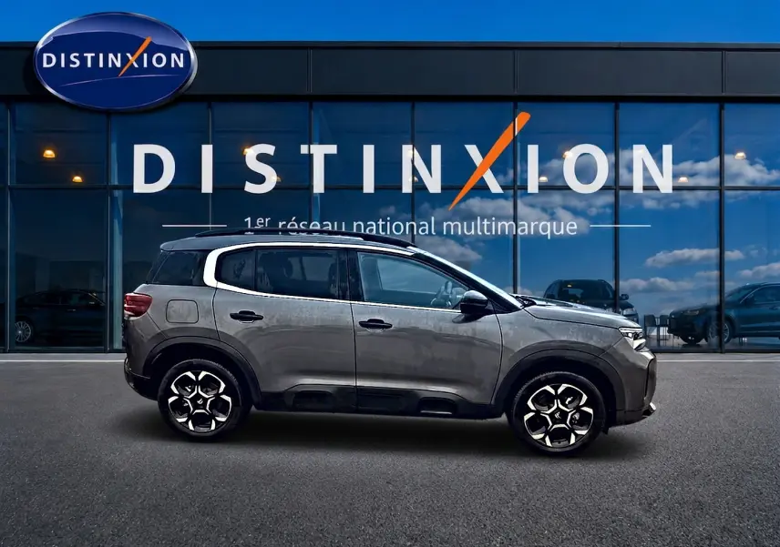Profil côté gauche d'un Citroën C5 Aircross gris 2025 avec jantes alu et vitres arrière teintées devant un showroom Distinxion.