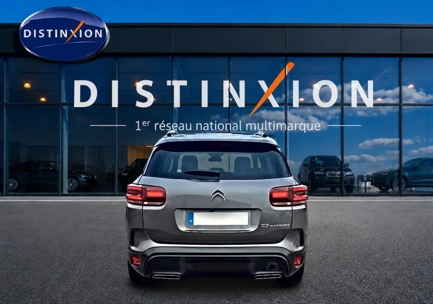 Vue arrière d'un Citroën C5 Aircross gris 2025 garé devant une vitrine avec logo Distinxion.