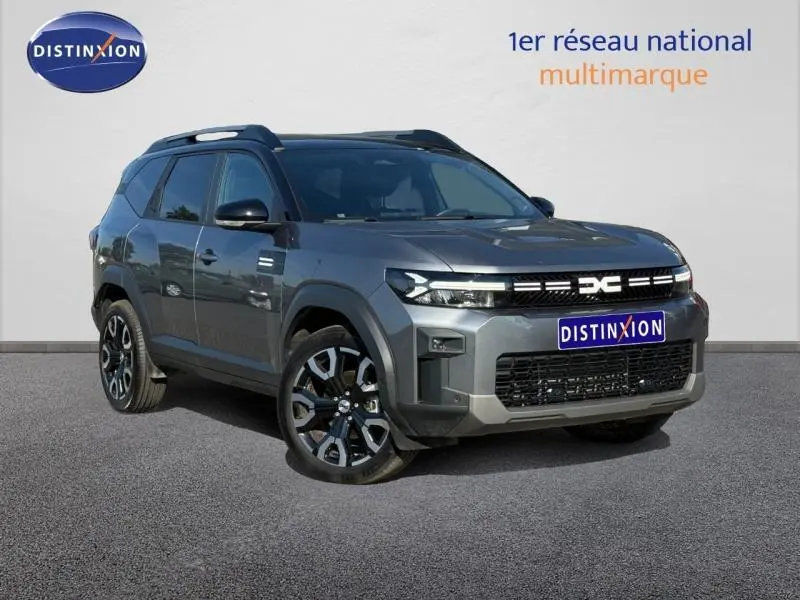 SUV Dacia Bigster gris schiste en 3/4 avant droit avec jantes alliage et barres de toit noires.