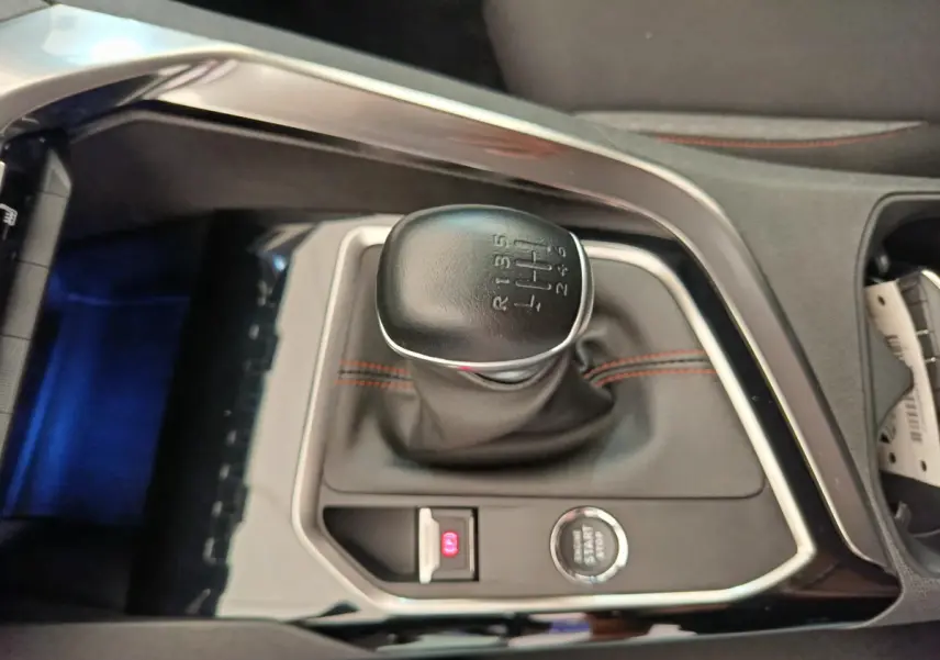 Gros plan sur le levier de vitesses manuel noir avec coutures rouges du Peugeot 3008 gris foncé, console centrale visible.