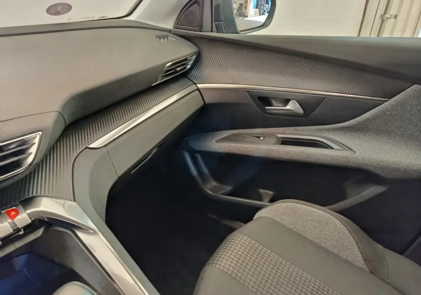 Intérieur côté passager du Peugeot 3008 gris foncé, avec tableau de bord texturé et siège tissu à motifs.