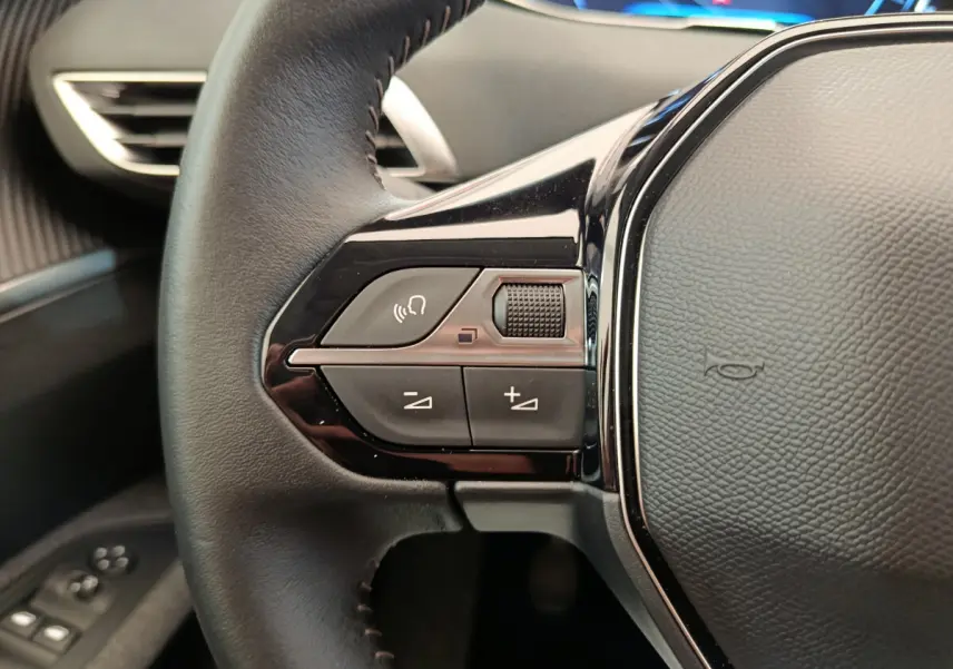 Gros plan sur le volant cuir noir du Peugeot 3008 2020, avec commandes audio et affichage numérique en arrière-plan.