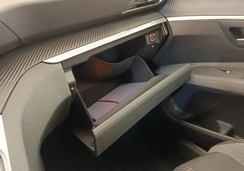Gros plan sur la boîte à gants ouverte côté passager du Peugeot 3008 gris foncé, montrant un livret à l'intérieur.