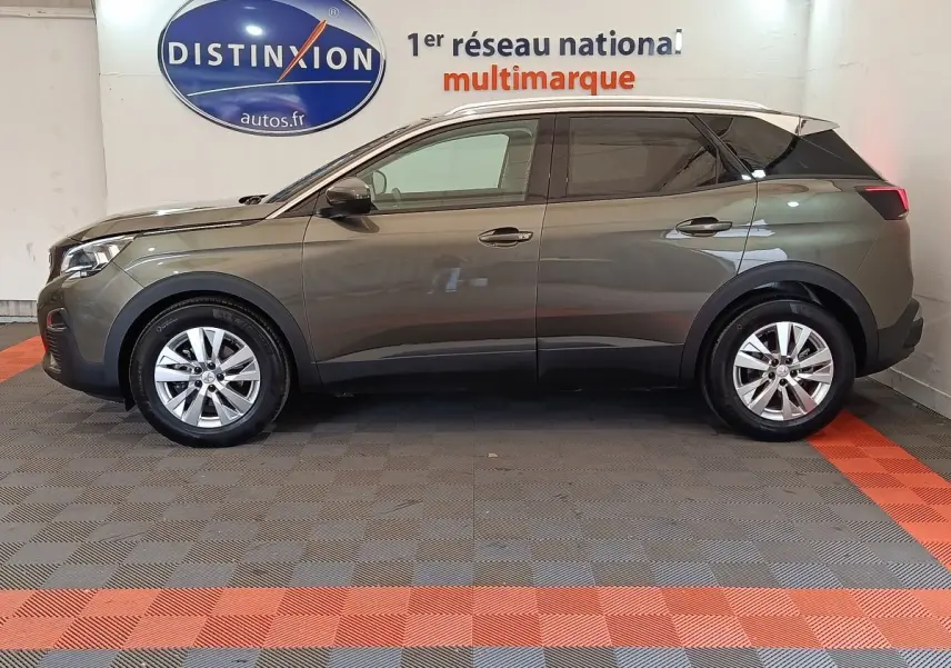 Profil côté gauche d'un Peugeot 3008 gris foncé 2020 garé en intérieur sur sol à damiers gris et orange.