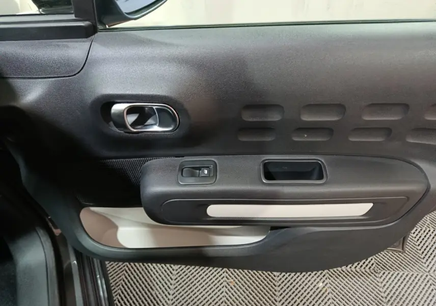Vue rapprochée de la porte avant gauche de la Citroën C3 gris foncé, avec poignée intérieure chromée et commandes électriques.