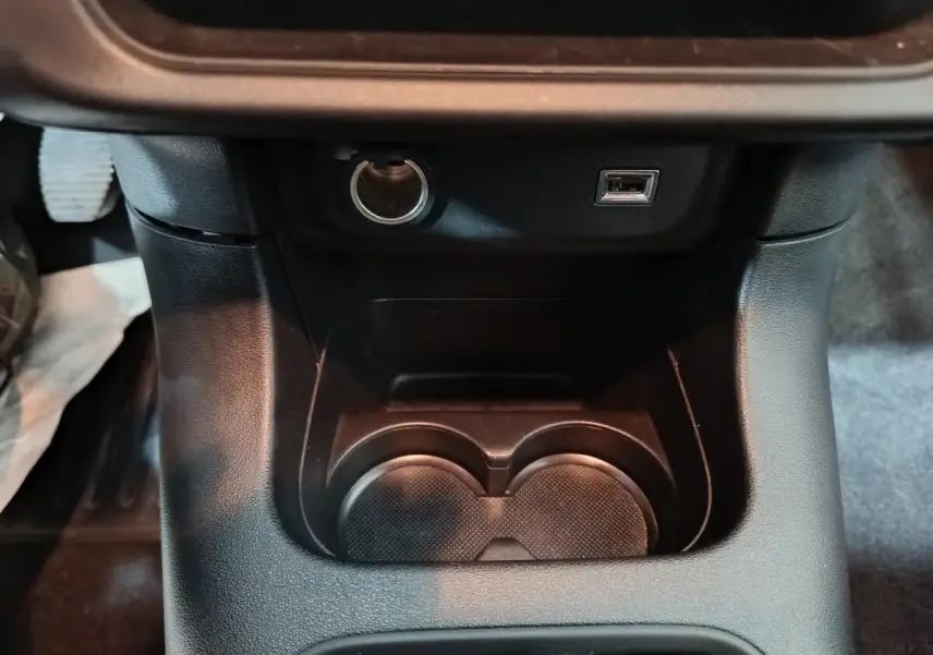 Gros plan sur la console centrale noire de la Citroën C3 2024, montrant porte-gobelets, prise 12V et port USB.