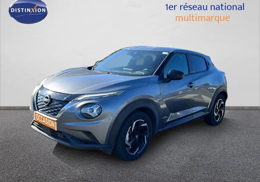 Nissan Juke Hybrid gris squale metal en 3/4 avant droit, avec jantes noires et détails noirs contrastants.