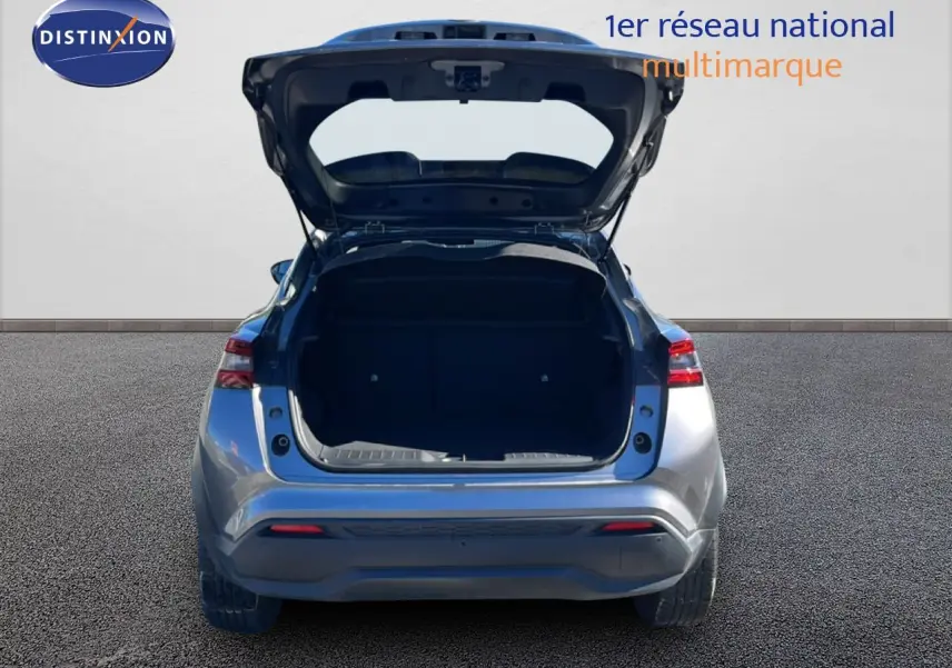 Vue arrière d'un Nissan Juke Hybrid gris squale métal 2024 avec coffre ouvert sur fond neutre.