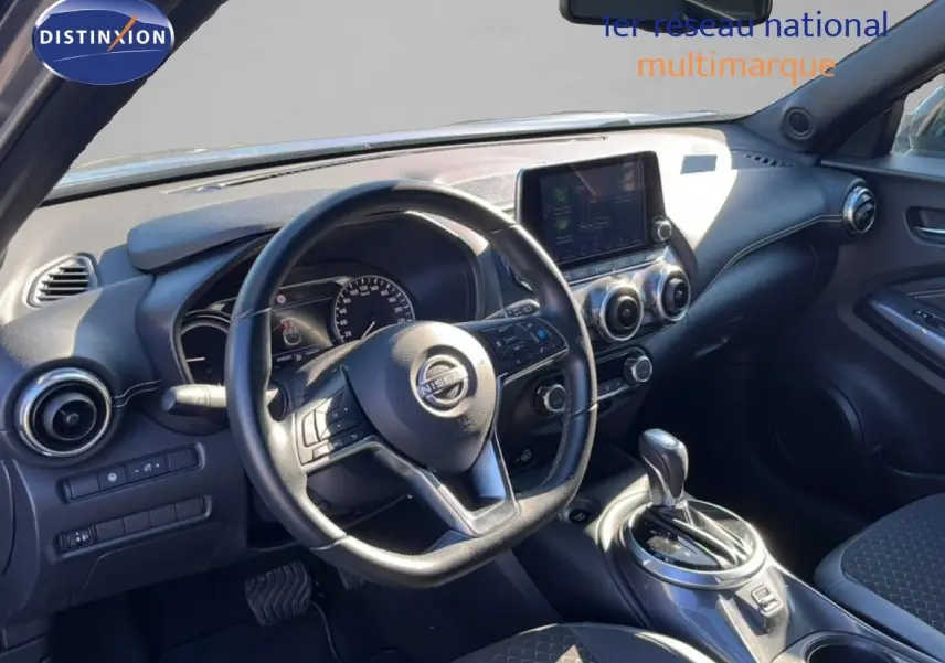 Vue intérieure du poste de conduite du Nissan Juke Hybrid 2024, avec volant multifonction et console centrale grise métallique.