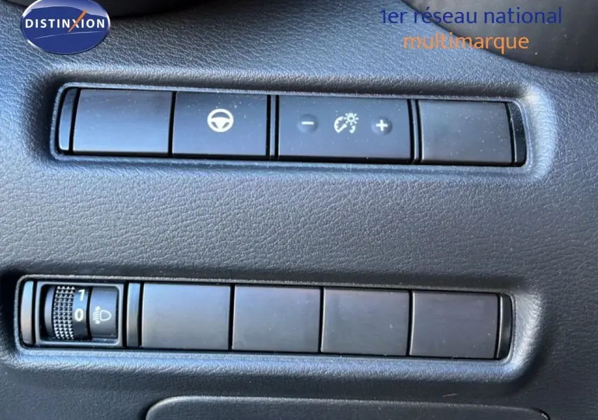 Gros plan sur les commandes de réglage de luminosité et assistance au volant du tableau de bord d’un Nissan Juke gris squale métal.