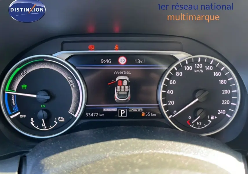 Tableau de bord du Nissan Juke Hybrid 2024 en gris, affichant compteurs et écran digital avec alertes et vitesse.